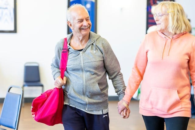 A smiling senior couple in athletic wear holding hands and walking together, representing longevity and vitality
