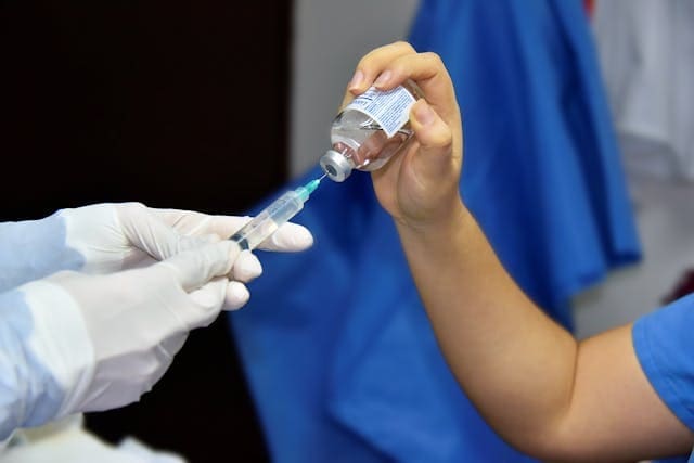 A close-up of a medical professional's gloved hands drawing clear liquid from a glass vial into a syringe for a treatment session.