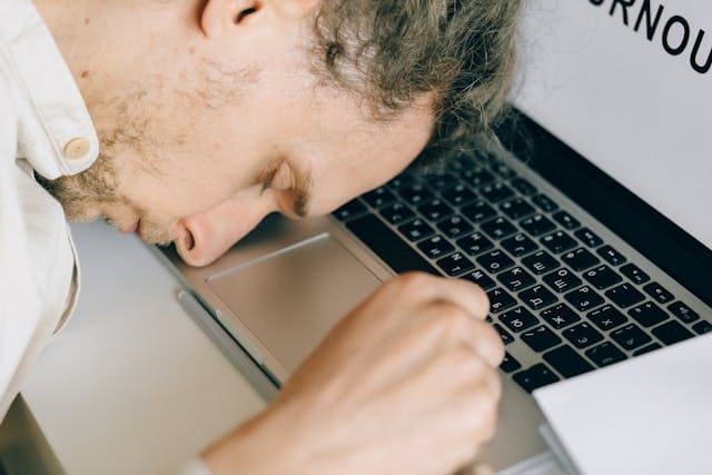 A man sitting at a desk with his head in his hands, appearing frustrated and mentally exhausted, representing symptoms of brain fog and difficulty concentrating