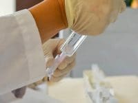 A physician's assistant in gloves preparing a stem cell solution by drawing it up from a multi-vial tray.
