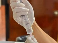 Clinical close-up of a medical professional carefully drawing a clear stem cell solution into a large syringe from a small vial.
