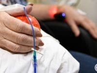 Patient holding an apple during Methylene Blue IV session with light therapy device visible on the wrist.