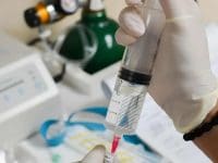 Hands in surgical gloves carefully prepare a dosage of mesenchymal stem cells (MSCs) for regenerative treatment with lab equipment nearby.