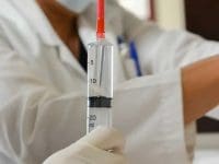 A nurse or doctor wearing a face mask holds a large syringe filled with mesenchymal stem cells, ready for the regenerative injection procedure.