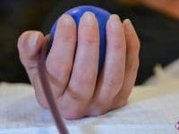 Close-up of a patient's hand squeezing a blue stress ball to maintain blood flow during the EBOO apheresis detoxification process.