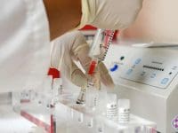 Gloved hand draws a sterile stem cell solution from a vial into a syringe in a medical laboratory setting.