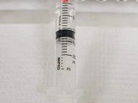 A 25ml syringe containing a clear stem cell solution, with a protective red cap, prepped for regenerative cell therapy.